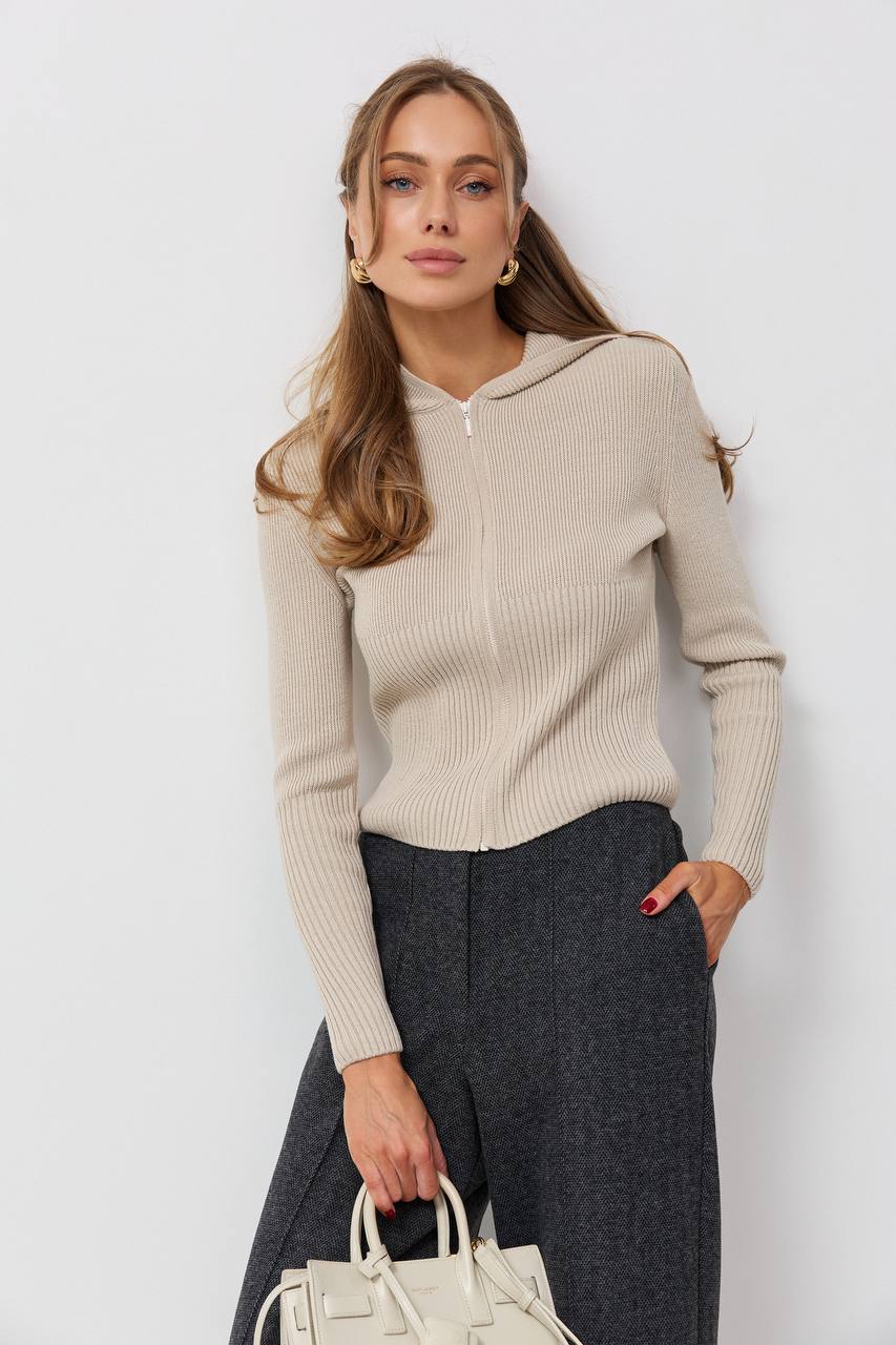 Woman wearing a beige sweater with a hood against a white background