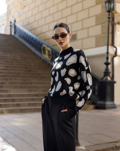 Woman wearing a black sweater with white patterns and black pants standing on steps outdoors.