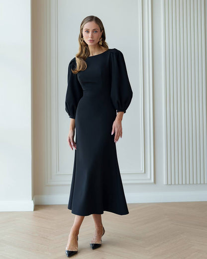 Woman wearing a black dress with puffed sleeves in an elegant room.