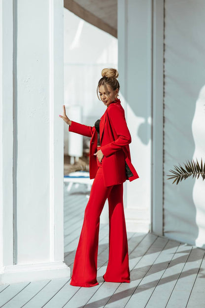 Woman in a red outfit standing on a wooden deck with white columns.