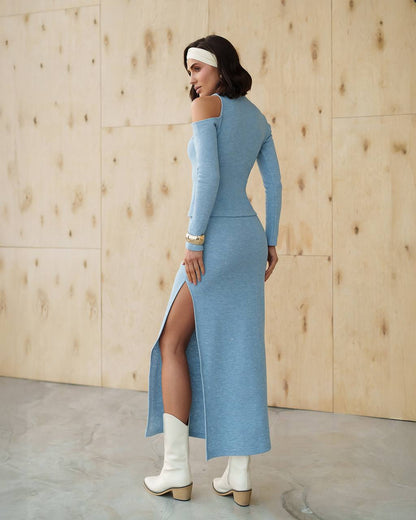 Woman wearing a blue dress with a high slit, standing against a wooden paneled wall.