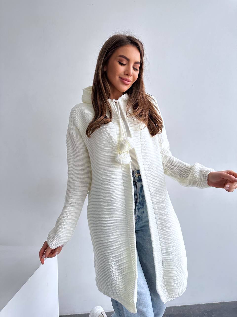 Woman wearing a long white cardigan with a hood against a plain background