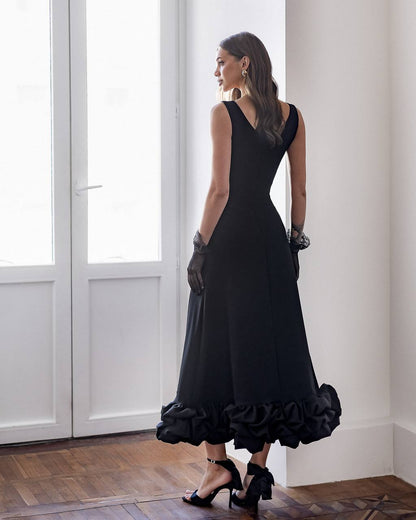 Woman in a black evening gown standing in a room with large windows.