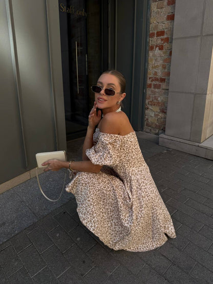 Woman in a floral off-shoulder dress sitting on a sidewalk.