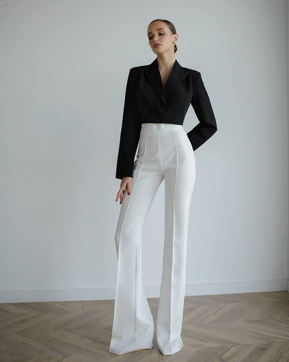 Woman wearing a black blazer and white pants against a plain background