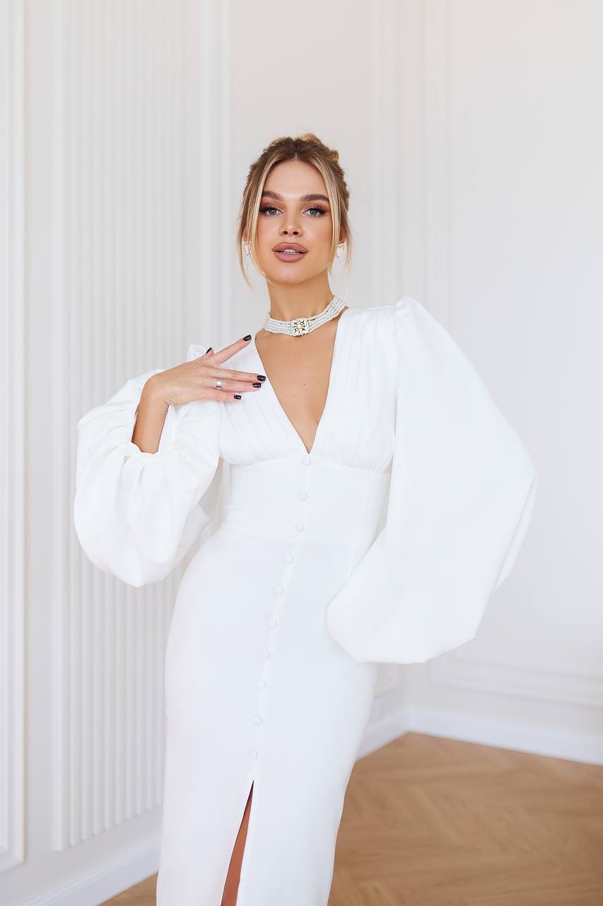 Woman wearing a white dress with puffed sleeves in a minimalistic room.