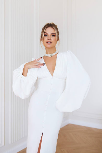 Woman wearing a white dress with puffed sleeves in a minimalistic room.