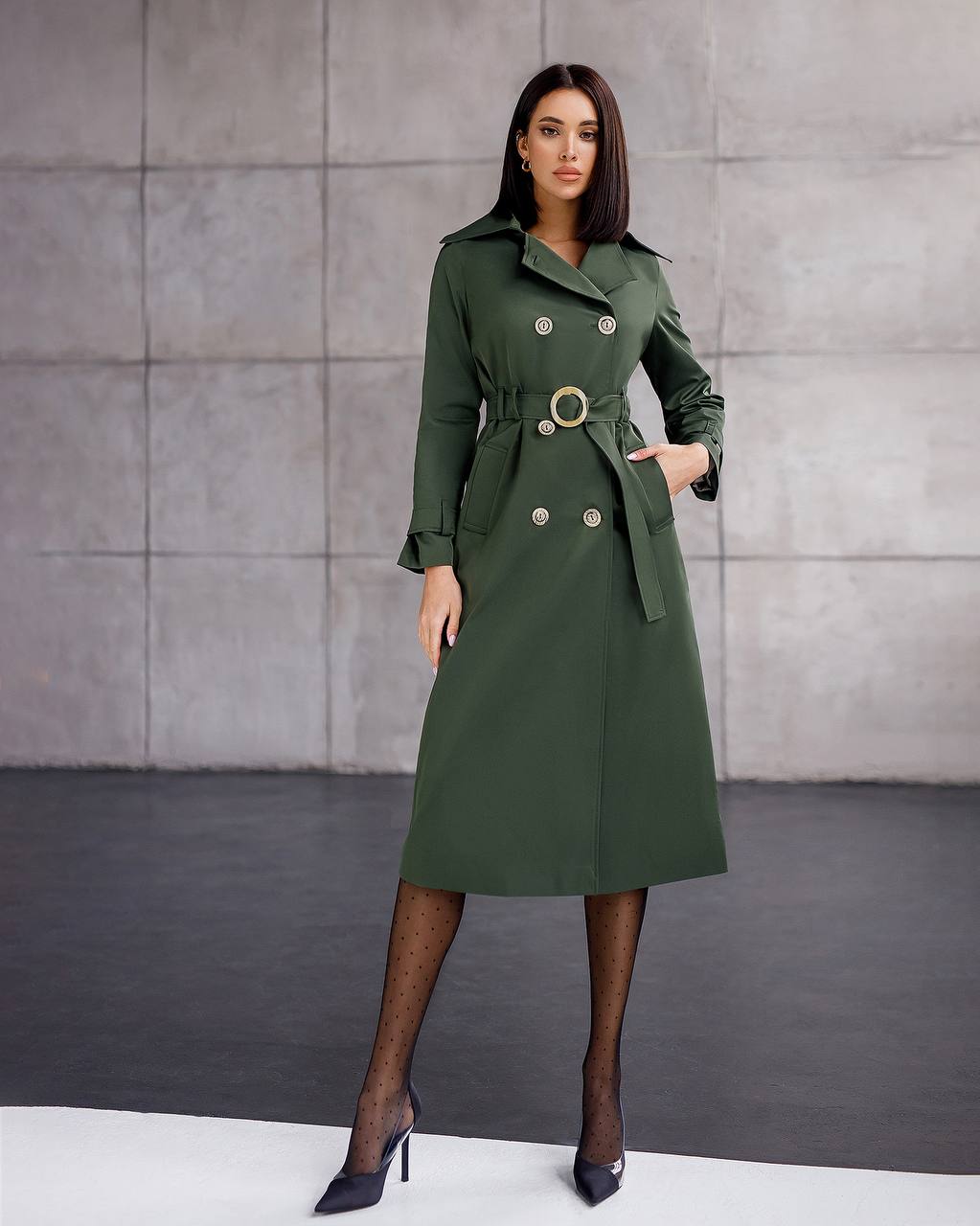 Woman wearing a green trench coat against a gray background