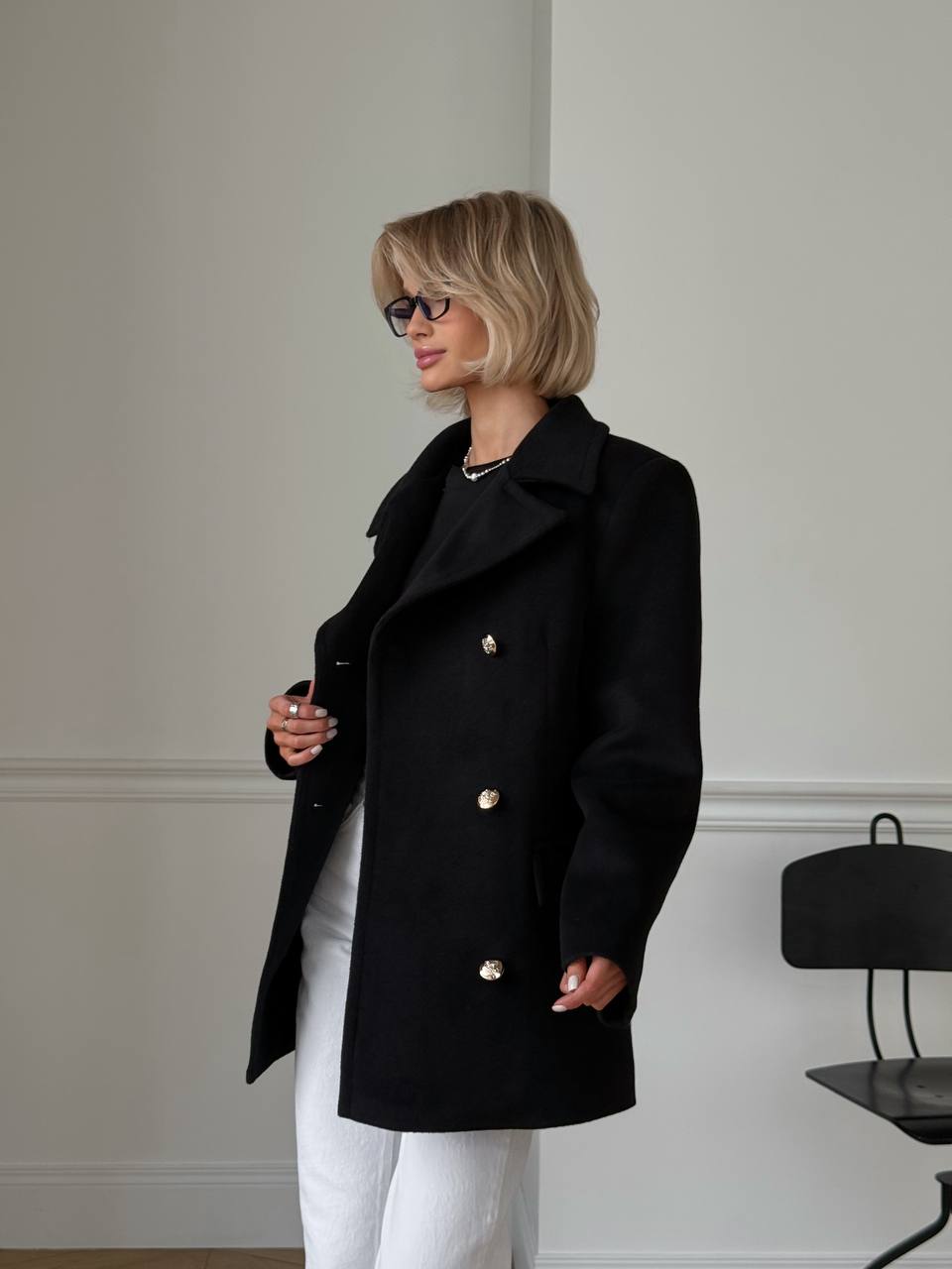 Woman wearing a black coat with gold buttons in an indoor setting