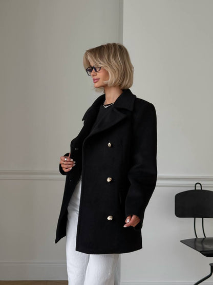 Woman wearing a black coat with gold buttons in an indoor setting