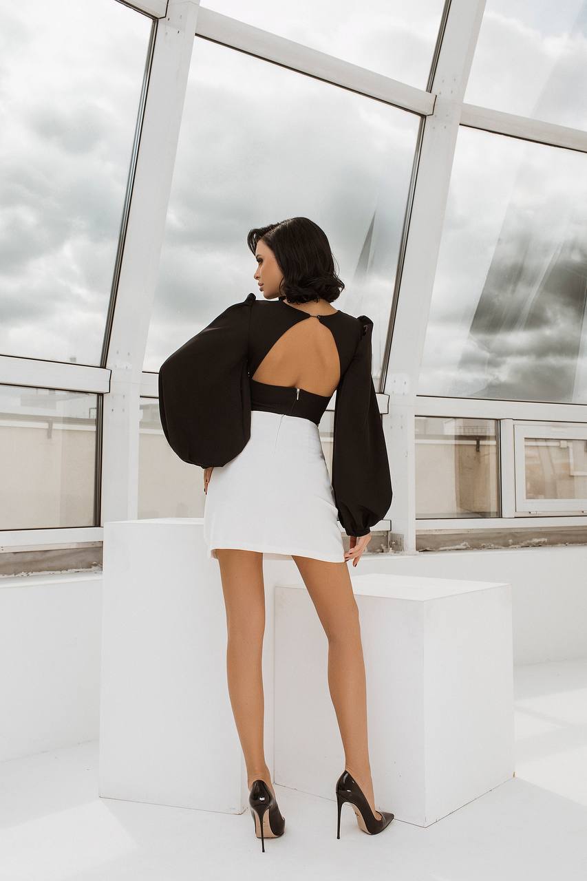Woman in a black top and white skirt standing in a modern indoor setting with large windows.