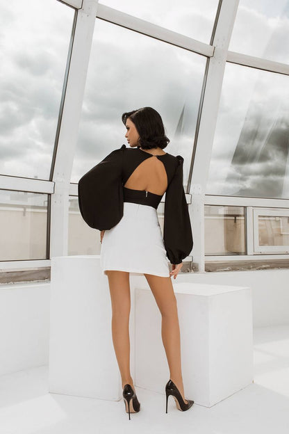 Woman in a black top and white skirt standing in a modern indoor setting with large windows.