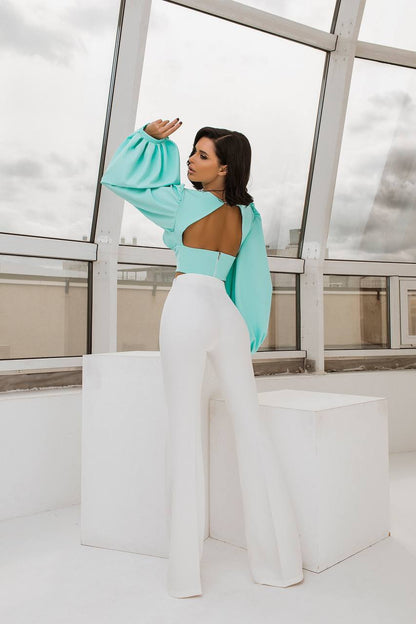 Woman in a turquoise top and white pants standing on a white platform with a glass wall background