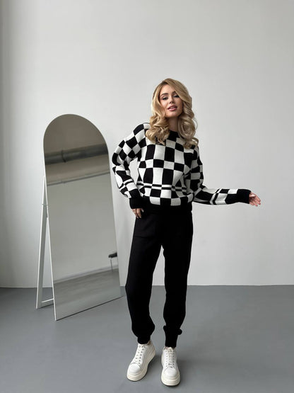Woman wearing a black and white checkered sweater and black pants standing in front of a mirror.