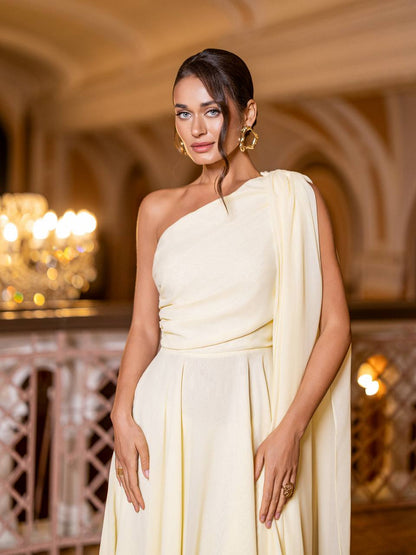 Woman in a light yellow one-shoulder dress standing in an elegant indoor setting.