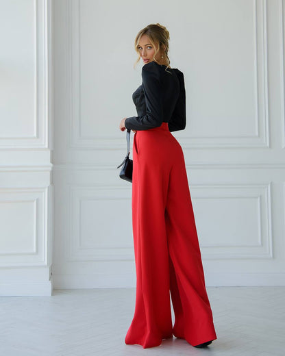 Person wearing a black top and red pants in a minimalistic setting