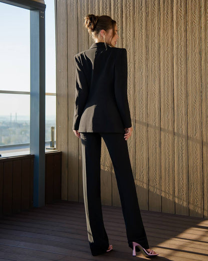 Woman in a black suit standing in a room with wooden floor and large window
