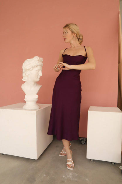 Woman in a burgundy dress standing next to a marble bust in a room with pink walls.