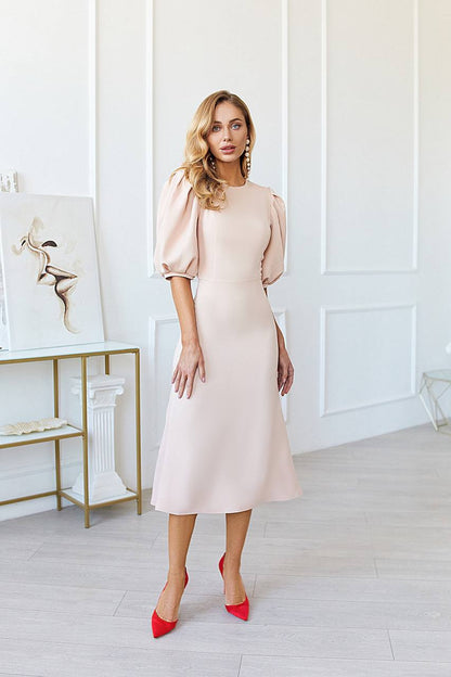 Woman in a light pink dress with red shoes standing in a stylish room.
