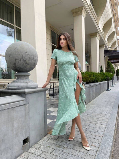Woman in a light green dress standing on a sidewalk with classical architecture in the background