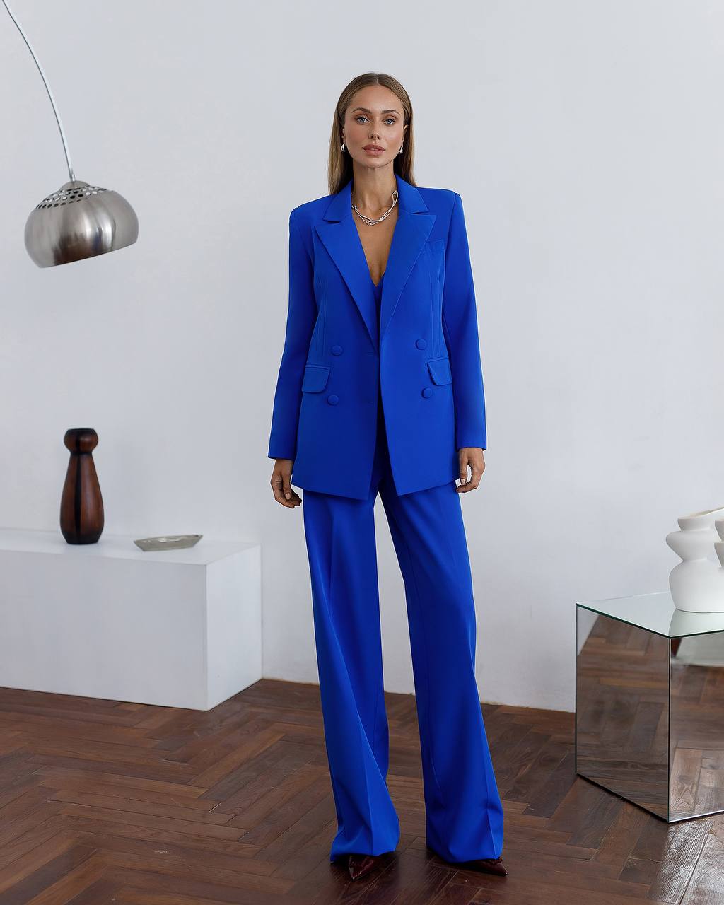 Woman wearing a blue suit standing in a modern room with minimal decor.