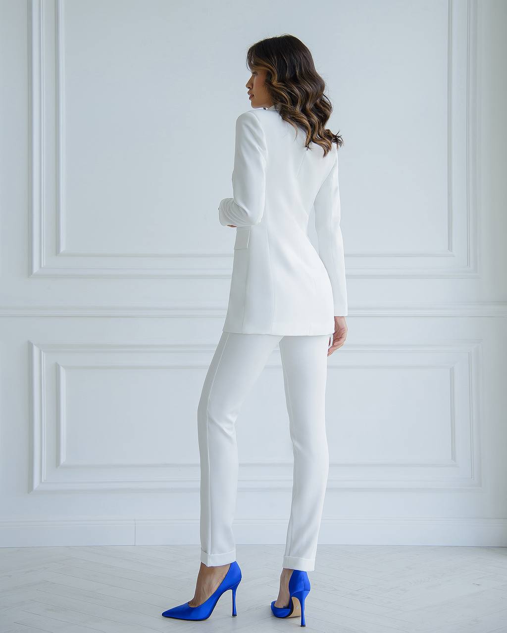 Woman wearing a white suit with blue high heels against a white wall
