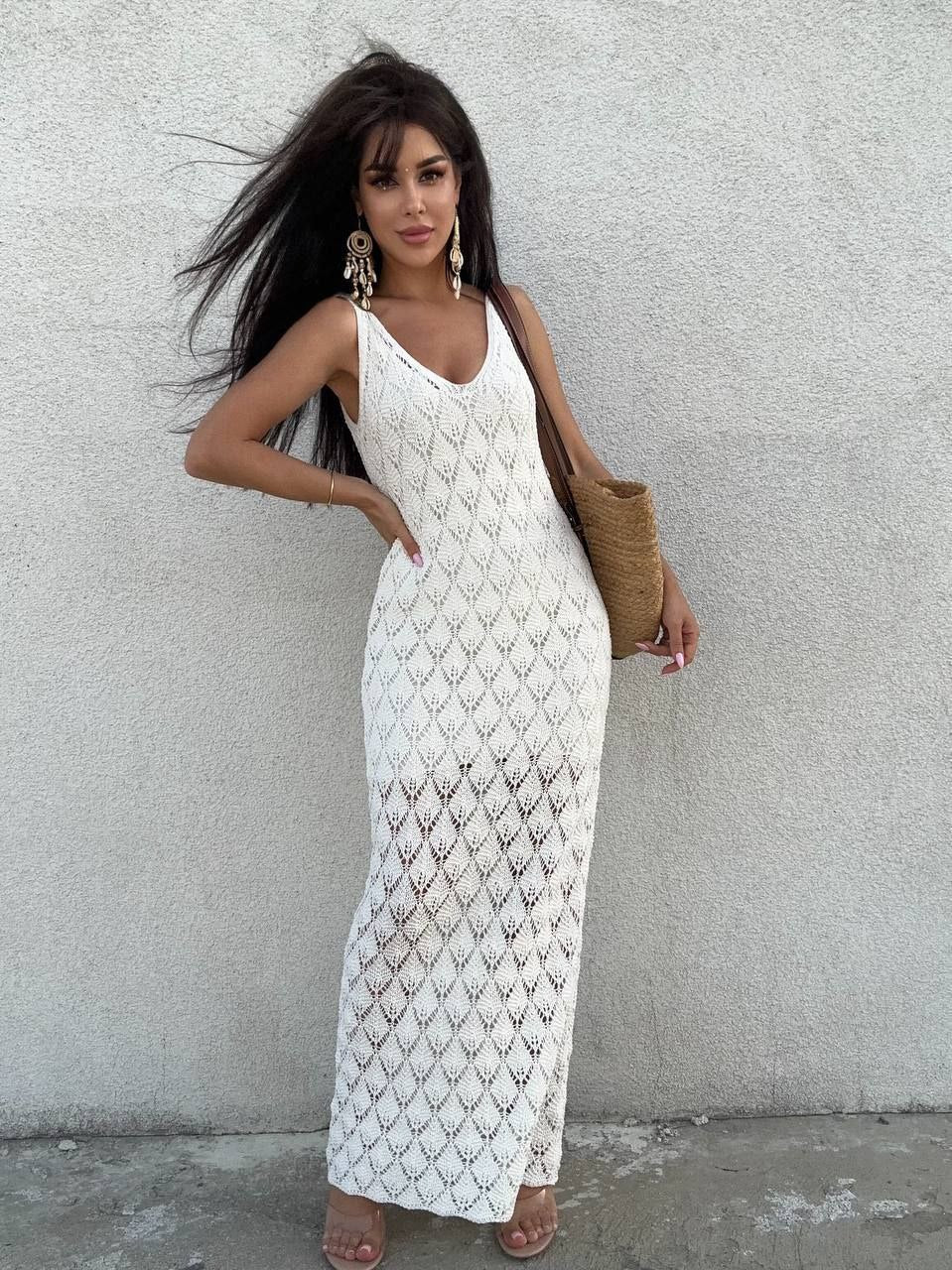 Woman wearing a white crochet dress against a gray wall