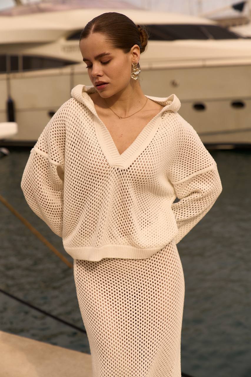 Woman wearing a beige knit outfit standing by a marina with boats in the background.
