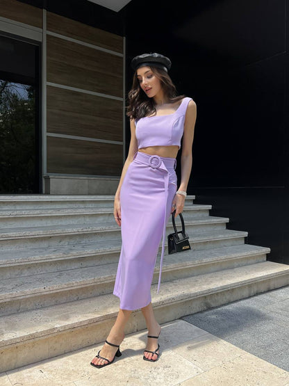 Woman in a lavender outfit standing on steps with a black background