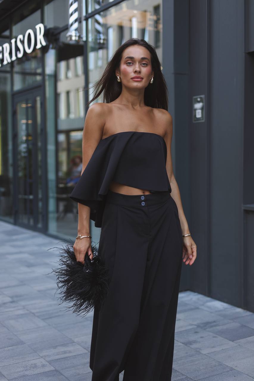 Woman wearing a black strapless top and wide-leg pants on a city street.