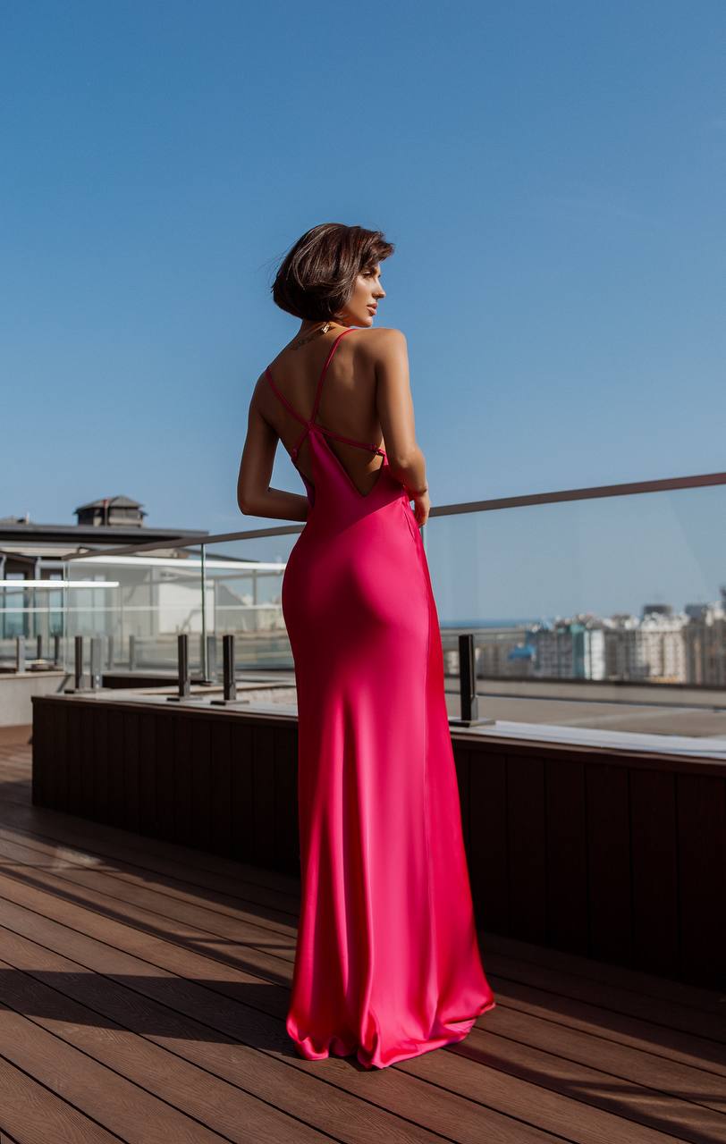 Woman in a pink evening gown standing on a rooftop with a clear blue sky.