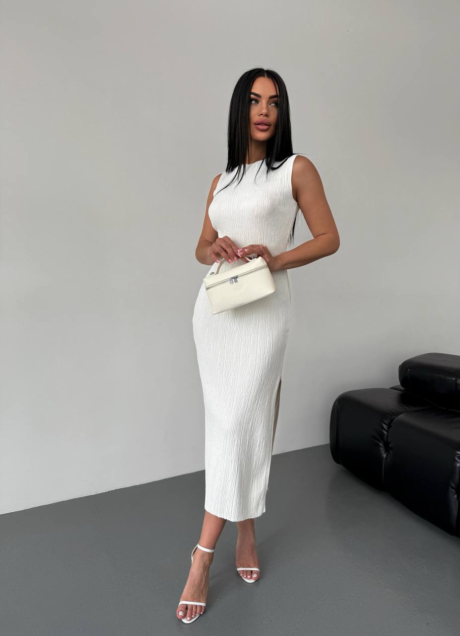 Woman in a white dress holding a clutch against a gray background