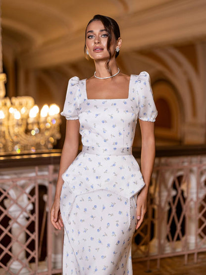 Woman in a white floral dress standing in an elegant indoor setting with chandeliers.