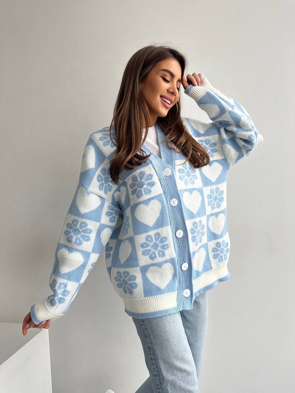 Woman wearing a light blue cardigan with heart and snowflake pattern on a plain background