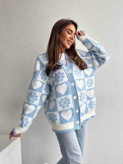 Woman wearing a light blue cardigan with heart and snowflake pattern on a plain background