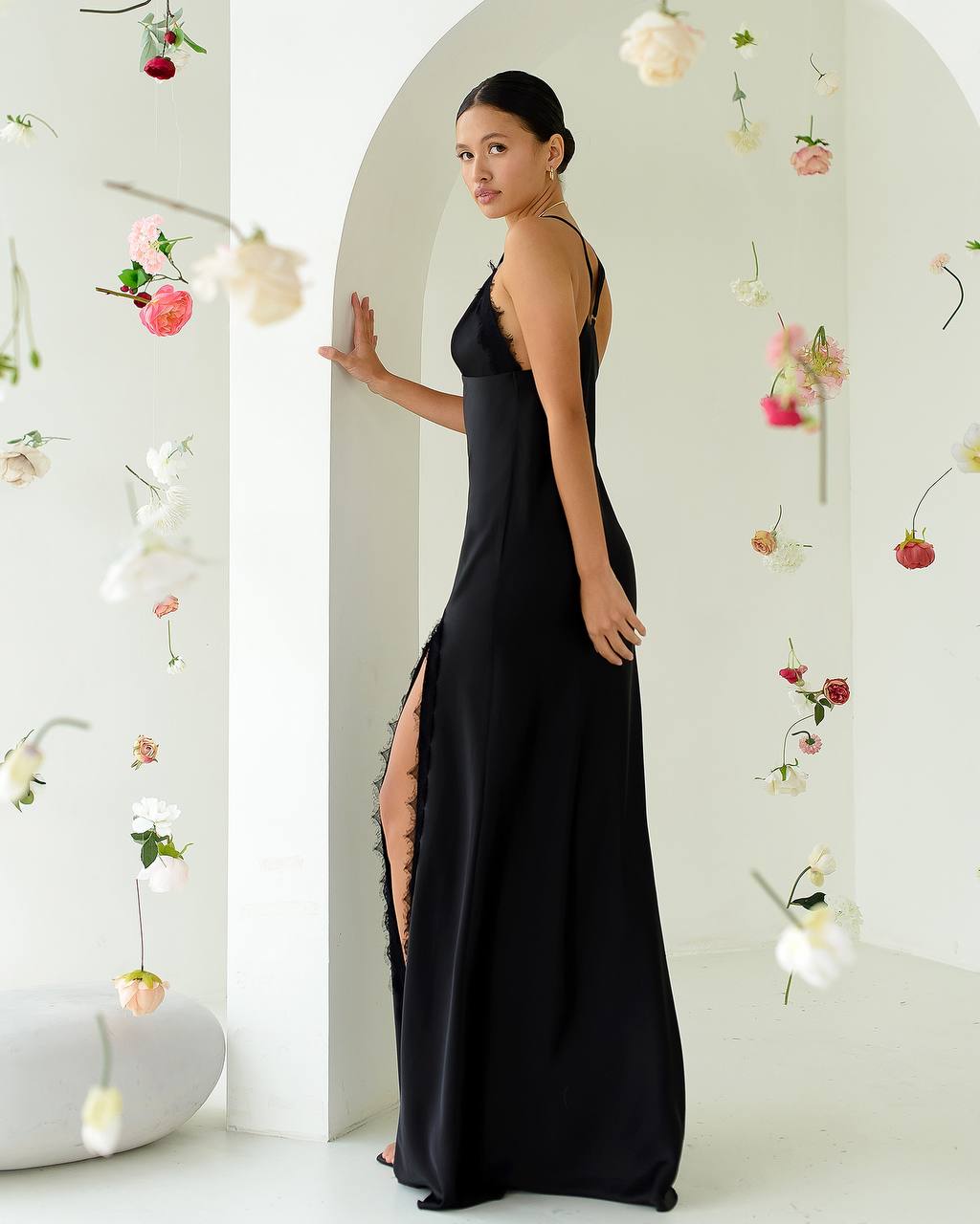 Woman in a black dress standing in a decorated room with flowers.