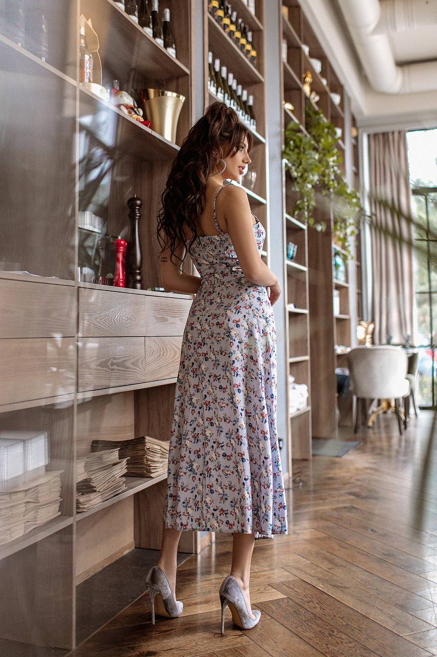 Woman in a floral dress standing in a modern interior setting with wooden shelves and decor.