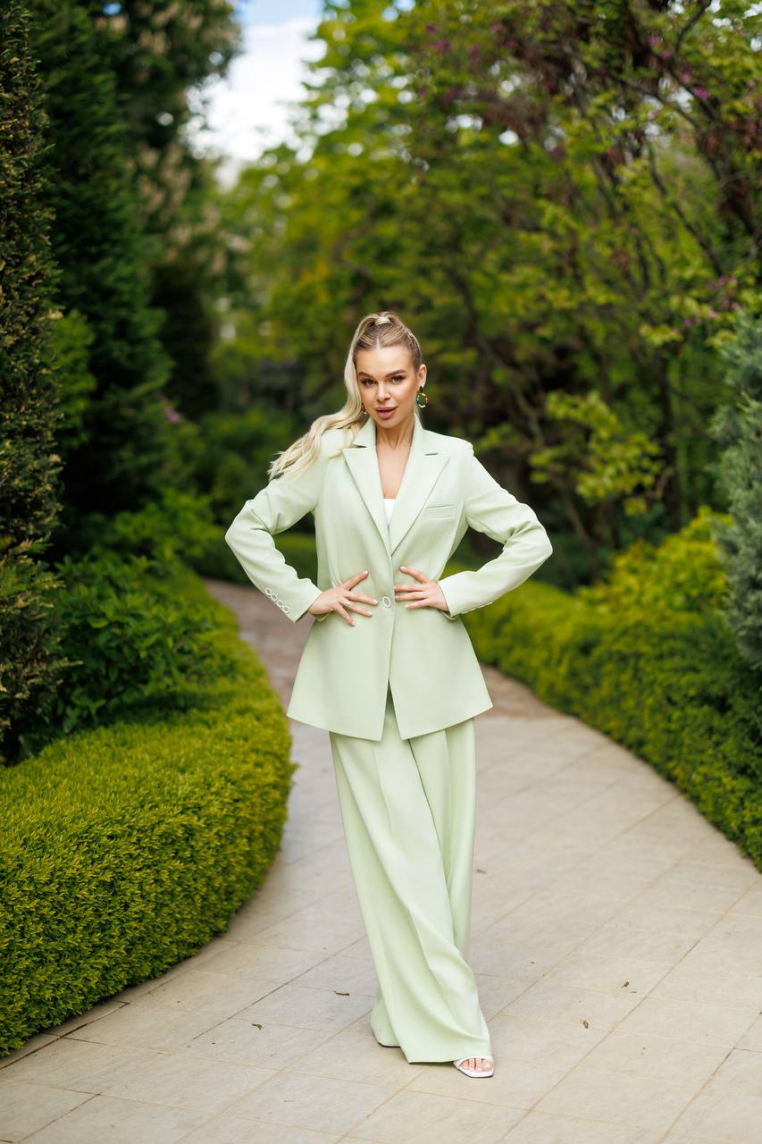 Woman in a light green suit standing on a path with greenery around