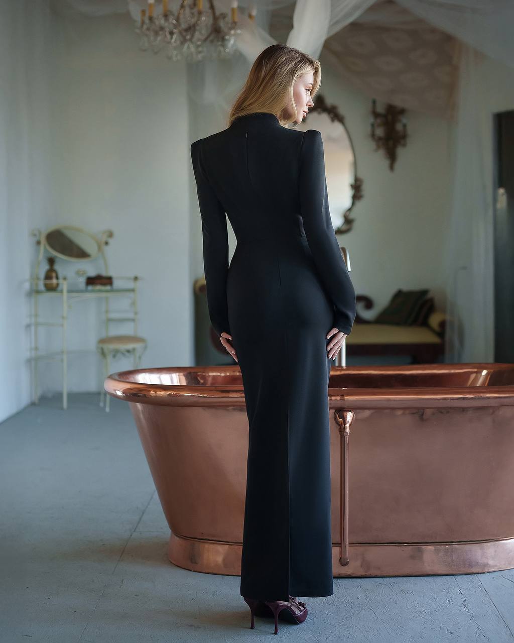 Woman in a black dress standing next to a copper bathtub in an elegant room.