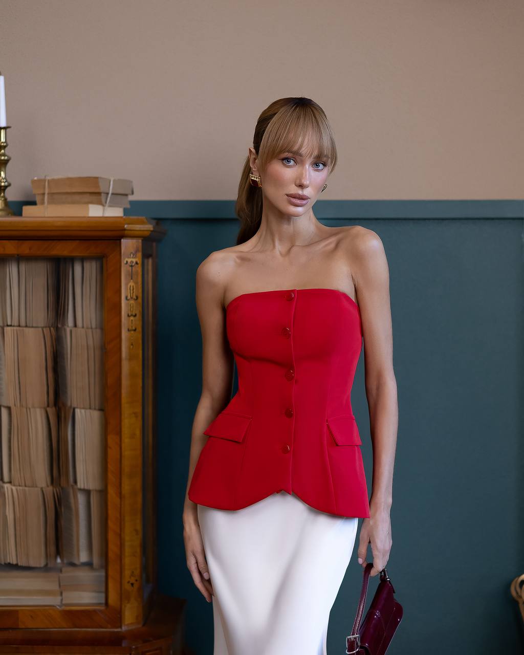 Woman wearing a red strapless top and white pants in an indoor setting.