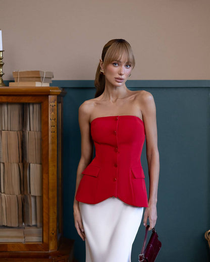Woman wearing a red strapless top and white pants in an indoor setting.
