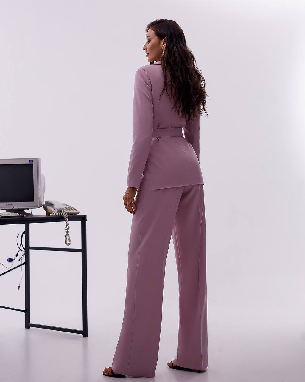 Woman in a mauve suit standing in an office setting with a white background