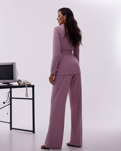 Woman in a mauve suit standing in an office setting with a white background