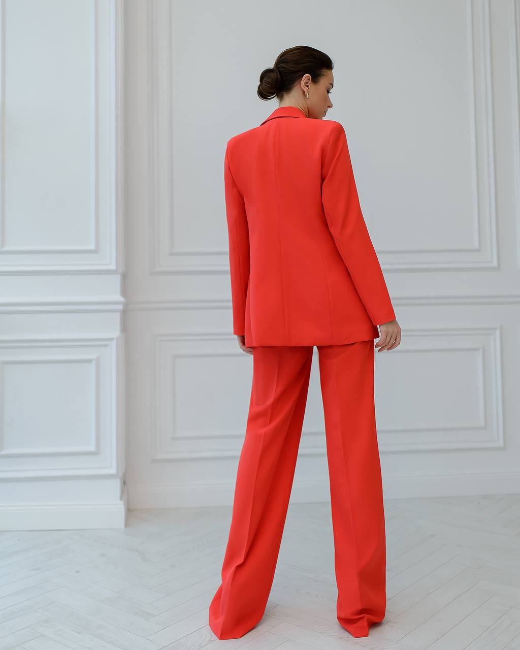 Woman wearing a bright red suit standing against a white paneled wall.