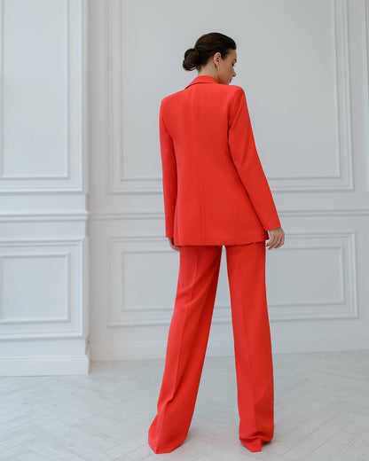 Woman wearing a bright red suit standing against a white paneled wall.