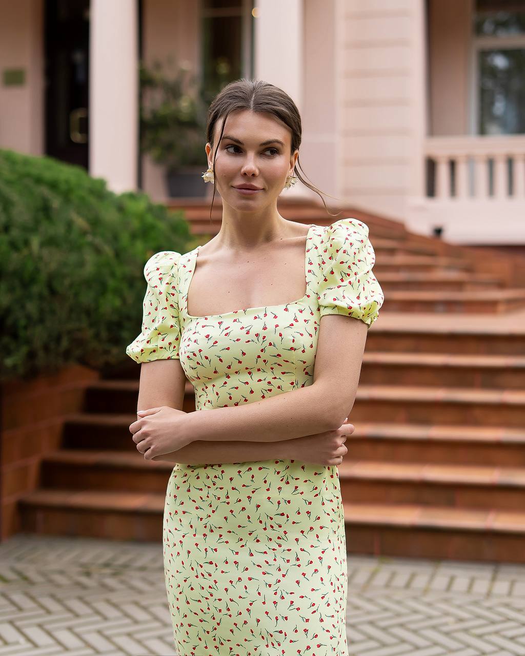 Woman in a light green dress with red pattern standing outdoors on steps.