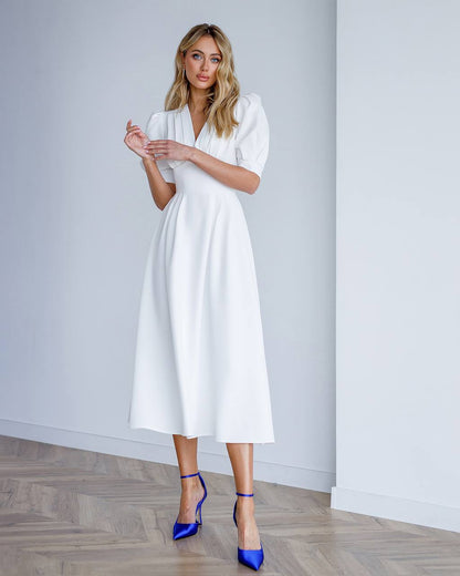 Woman wearing a white dress with puffed sleeves against a plain background
