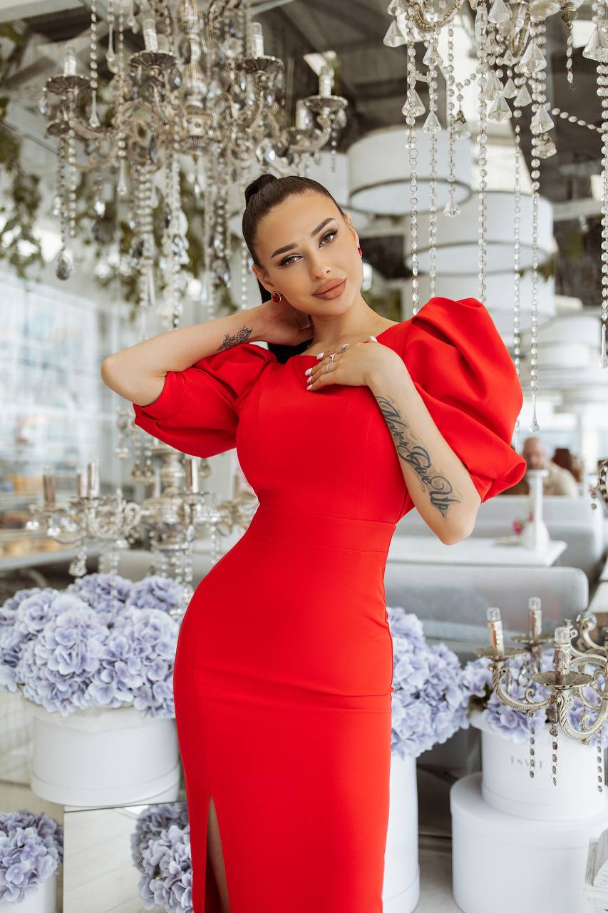 Woman in a red dress posing in an elegant indoor setting with chandeliers and floral arrangements.