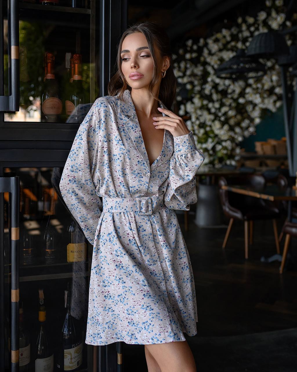 Woman in a floral dress standing in a dimly lit room with decorative elements.