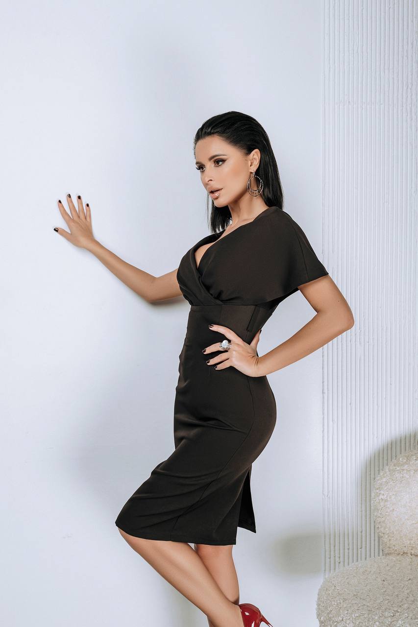 Woman wearing a black dress posing against a white wall.